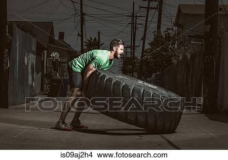 Young adult man lifting large tire, crossfit exercise View Large Photo Image Picture - Young adult man lifting large tire, crossfit exercise. Fotosearch
