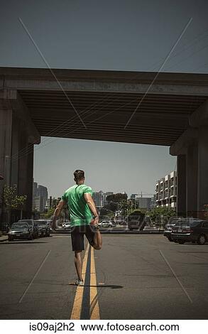 Stock Image - Young adult man stretching in road, rear view. Fotosearch