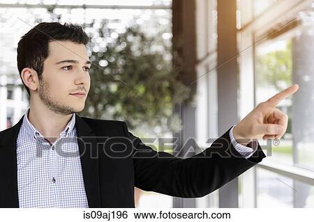 Young businessman pointing out of office window View Large Photo Image Stock Photograph - Young businessman pointing out of office window. Fotosearch