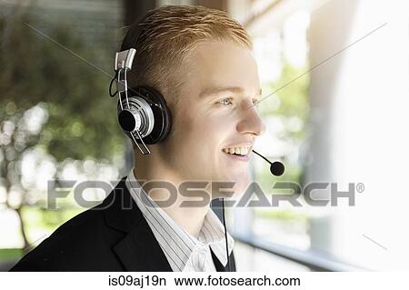 Young businessman using telephone headset and looking out of window View Large Photo Image Picture - Young businessman using telephone headset and looking out of window. Fotosearch