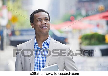 Stock Photograph - Young businessman walking on city street carrying digital pad. Fotosearch
