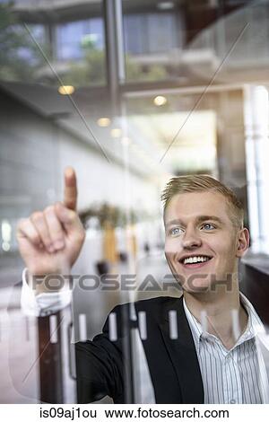Stock Photograph - Young businessman writing message on glass wall with finger. Fotosearch