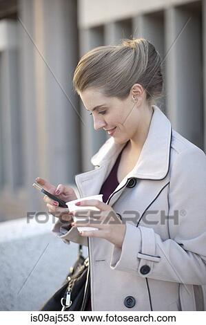Stock Image - Young businesswoman texting on smartphone in city. Fotosearch