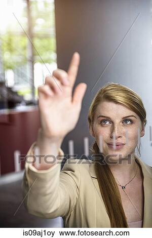 Stock Photo - Young businesswoman writing message on glass wall with finger. Fotosearch