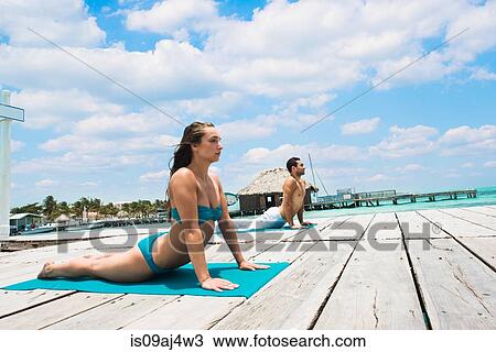 Stock Image - Young couple in cobra pose on pier, San Pedro, Belize. Fotosearch