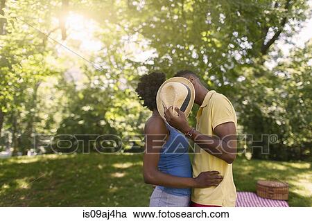 Young couple in park holding up hat to cover faces View Large Photo Image Stock Image - Young couple in park holding up hat to cover faces. Fotosearch