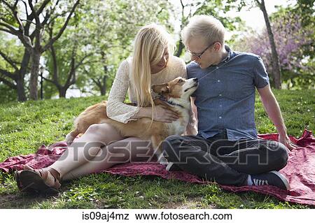 Stock Photo - Young couple with corgi dog sitting in park. Fotosearch