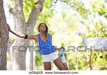 Stock Photograph - Young female runner warming up in park. Fotosearch