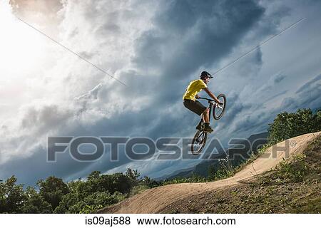 Stock Photo - Young male mountain biker jumping mid air on rural pump track. Fotosearch