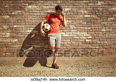 Young male soccer player chatting on smartphone on wasteland View Large Photo Image Stock Image - Young male soccer player chatting on smartphone on wasteland. Fotosearch