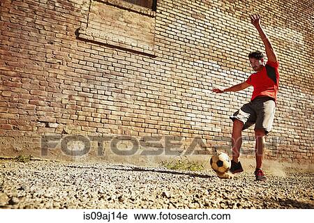 Stock Image - Young man playing soccer on wasteland. Fotosearch