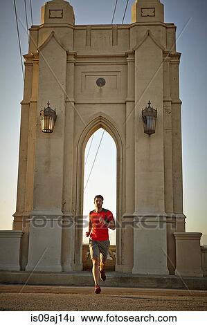 Young man running across city bridge View Large Photo Image Stock Photograph - Young man running across city bridge. Fotosearch