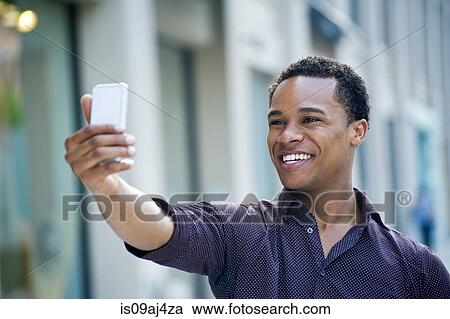 Stock Image - Young man taking smartphone selfie on city street. Fotosearch