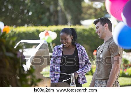 Picture - Young woman barbecuing with male soldier at homecoming party. Fotosearch
