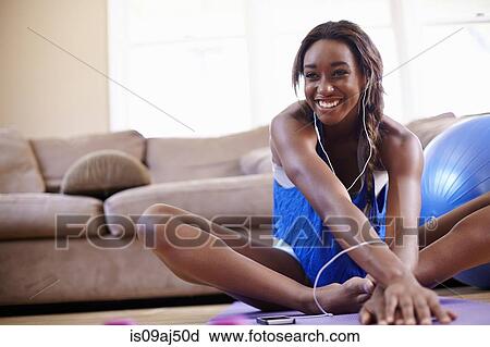Stock Image - Young woman exercising and stretching on sitting room floor. Fotosearch