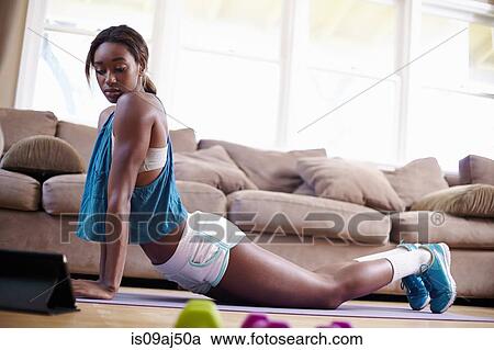 Young woman exercising on sitting room floor whilst looking at instruction on digital tablet View Large Photo Image Stock Image - Young woman exercising on sitting room floor whilst looking at instruction on digital tablet. Fotosearch