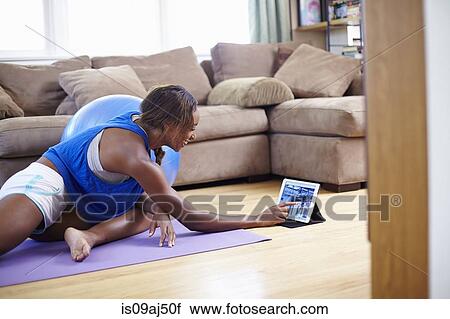 Young woman exercising on sitting room floor whilst using touchscreen on digital tablet View Large Photo Image Stock Image - Young woman exercising on sitting room floor whilst using touchscreen on digital tablet. Fotosearch
