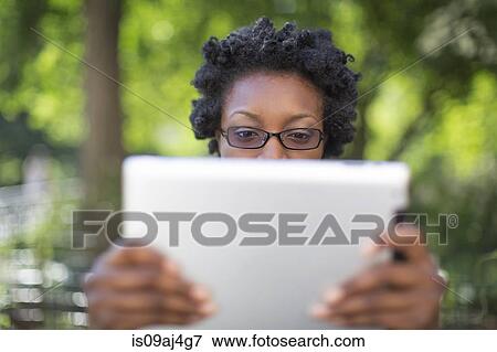 Young woman in park holding up and reading digital tablet View Large Photo Image Stock Photo - Young woman in park holding up and reading digital tablet. Fotosearch