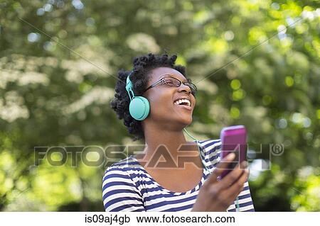 Young woman in park listening and singing to music on headphones View Large Photo Image Stock Image - Young woman in park listening and singing to music on headphones. Fotosearch