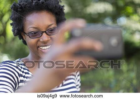 Young woman in park taking selfie on digital camera View Large Photo Image Stock Photo - Young woman in park taking selfie on digital camera. Fotosearch