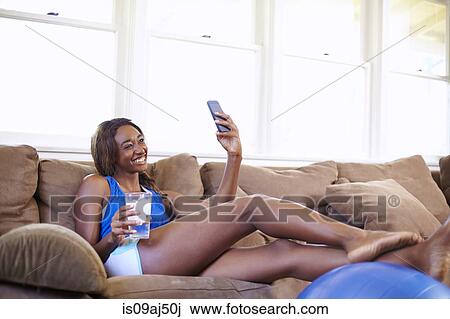Stock Image - Young woman on a training break, looking at smartphone in sitting room. Fotosearch
