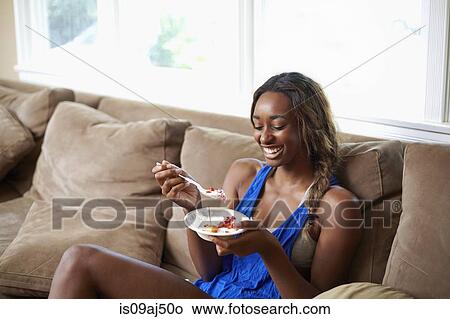Young woman taking a training break, eating fruit on sofa View Large Photo Image Picture - Young woman taking a training break, eating fruit on sofa. Fotosearch