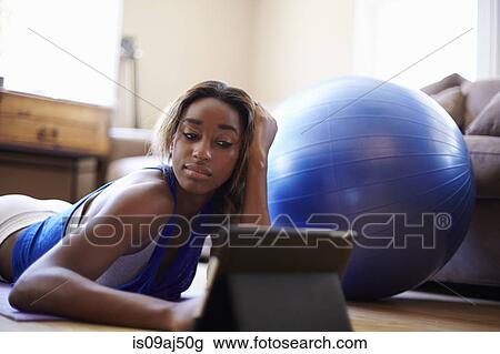 Stock Image - Young woman taking a training break, using digital tablet in sitting room. Fotosearch