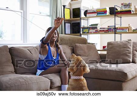 Stock Photo - Young woman taking a training break, holding up biscuit for dog in sitting room. Fotosearch