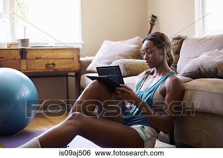 Young woman taking a training break, looking at digital tablet in sitting room View Large Photo Image Stock Photograph - Young woman taking a training break, looking at digital tablet in sitting room. Fotosearch