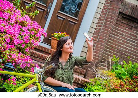 Stock Photograph - Young woman taking selfie on smartphone on house steps. Fotosearch