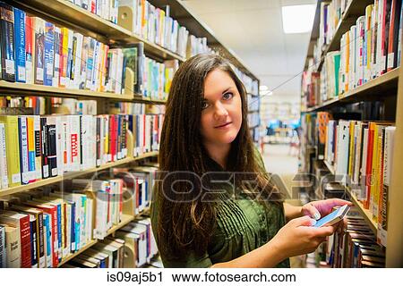 Stock Image - Young woman texting on smartphone in library. Fotosearch