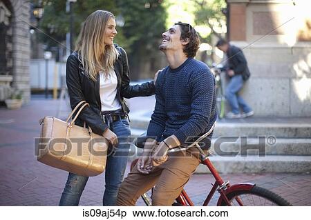 Stock Photography - Young woman with boyfriend leaning on bicycle, Cape Town, South Africa. Fotosearch