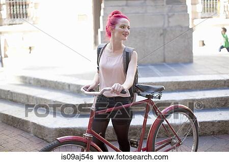 Stock Photograph - Young woman with pink hair pushing her bicycle in city. Fotosearch