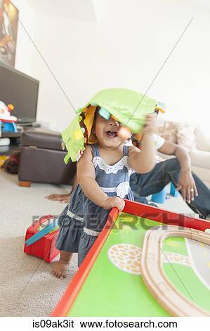Stock Photograph - Baby girl playing, father in background. Fotosearch