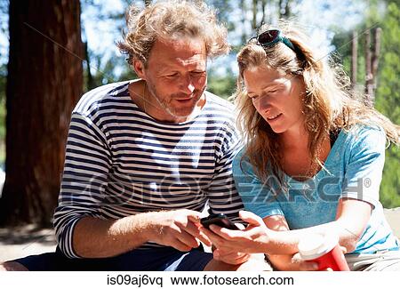 Couple looking down at smartphone in forest View Large Photo Image Stock Photography - Couple looking down at smartphone in forest. Fotosearch