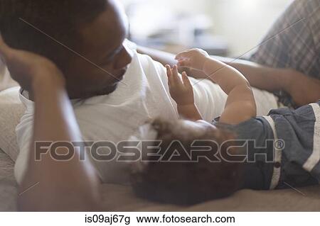 Stock Image - Father lying with baby daughter. Fotosearch