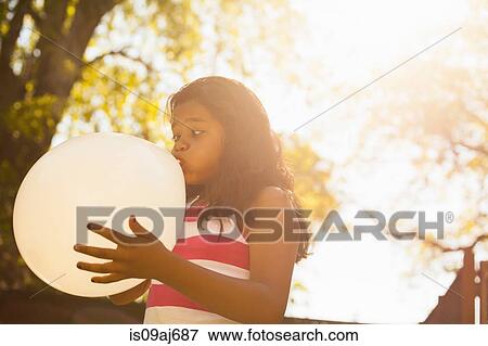 Stock Photo - Girl blowing up balloon in garden. Fotosearch