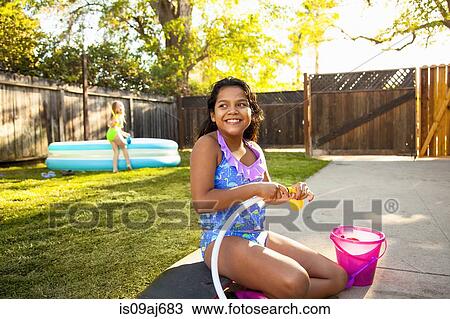 Stock Image - Girl filling balloon with water in garden. Fotosearch