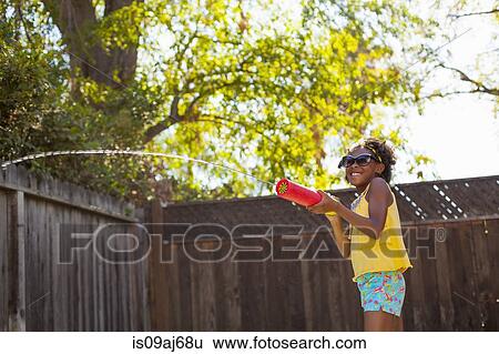 Girl spraying water from water gun in garden View Large Photo Image Stock Photograph - Girl spraying water from water gun in garden. Fotosearch
