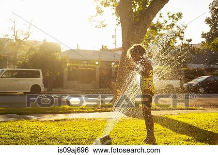 Girl standing in garden sprinkler View Large Photo Image Stock Photograph - Girl standing in garden sprinkler. Fotosearch