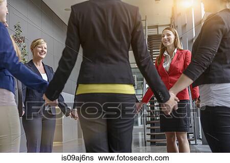 Stock Photograph - Group of businesswomen and men holding hands in circle. Fotosearch