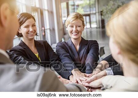 Stock Image - Group of businesswomen and men in a circle with hands together. Fotosearch