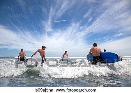 Group of male and female surfer friends wading into sea with surf boards View Large Photo Image Stock Image - Group of male and female surfer friends wading into sea with surf boards. Fotosearch
