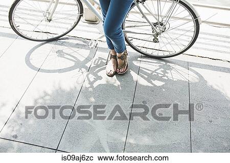 Stock Image - Legs of mid adult woman cyclist and bicycle. Fotosearch
