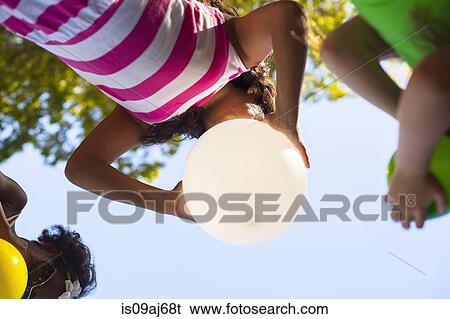 Stock Photograph - Low angle view of three girls inflating balloons in garden. Fotosearch