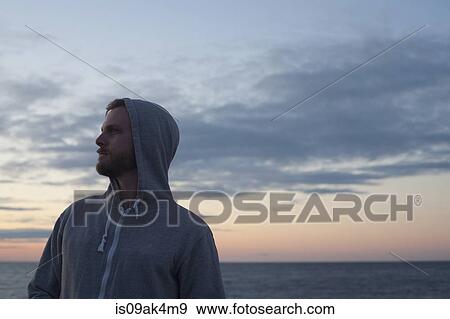 Mid adult man in hooded top gazing over his shoulder at coast, Gloucester, Massachusetts, USA View Large Photo Image Stock Photo - Mid adult man in hooded top gazing over his shoulder at coast, Gloucester, Massachusetts, USA. Fotosearch