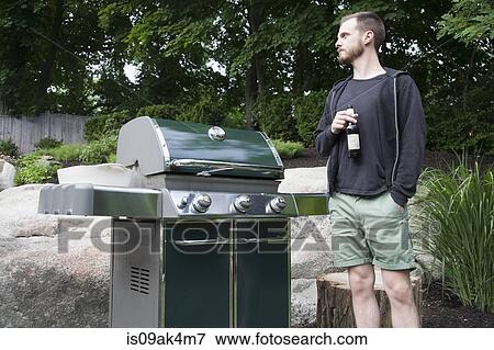 Mid adult man standing by barbecue with bottle of beer in garden View Large Photo Image Stock Photo - Mid adult man standing by barbecue with bottle of beer in garden. Fotosearch