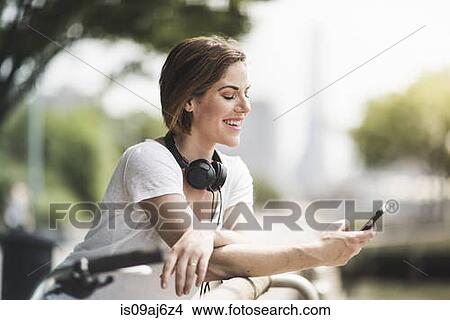 Mid adult woman cyclist looking at texts on her smartphone View Large Photo Image Picture - Mid adult woman cyclist looking at texts on her smartphone. Fotosearch