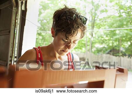 Stock Image - Mid adult woman restoring furniture in garage. Fotosearch