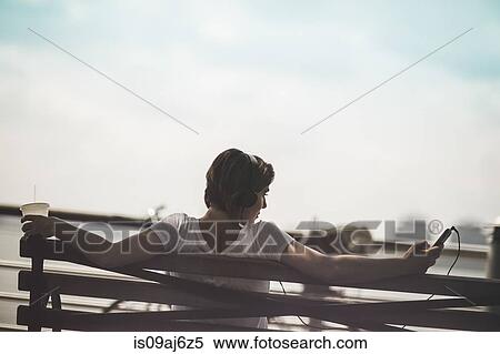 Mid adult woman sitting on bench with smartphone at riverside, New York City, USA View Large Photo Image Stock Photography - Mid adult woman sitting on bench with smartphone at riverside, New York City, USA. Fotosearch